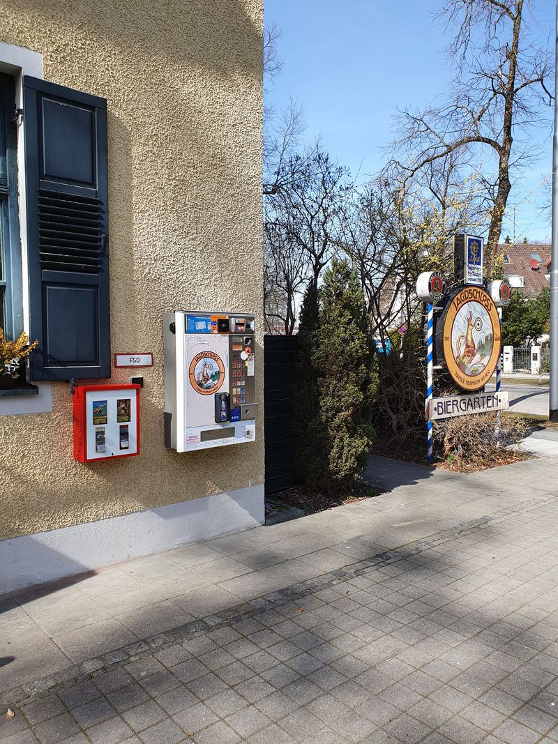 Kleiner roter Wandautomat neben einem Zigarettenautomaten an einer Hauswand