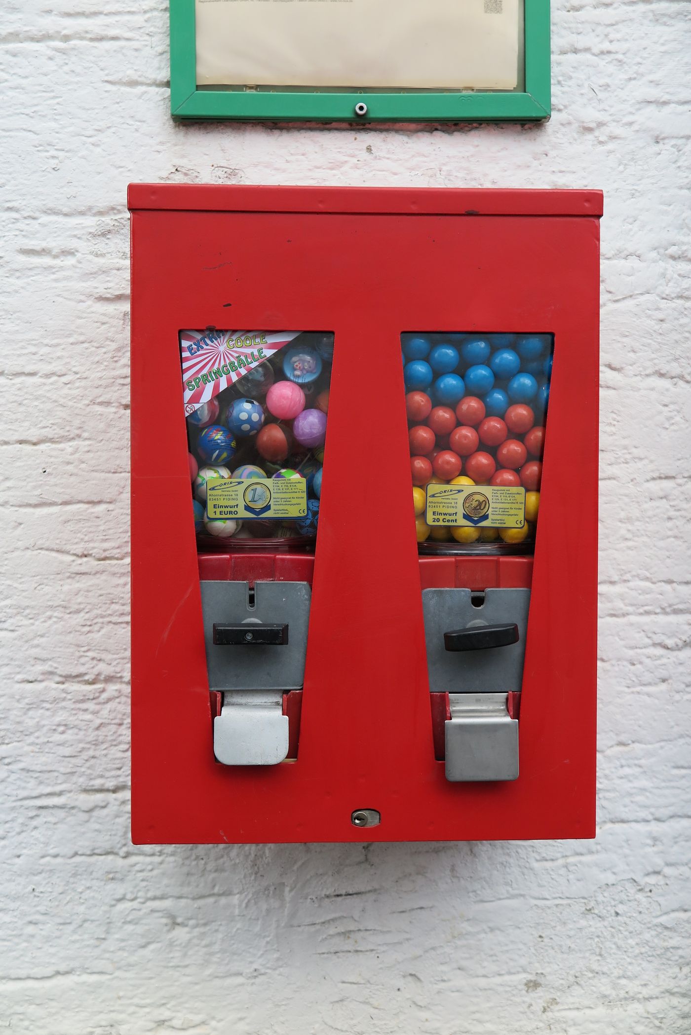 Roter Doppelautomat mit Springbällen und bunten Kaugummikugeln an weißer Wand