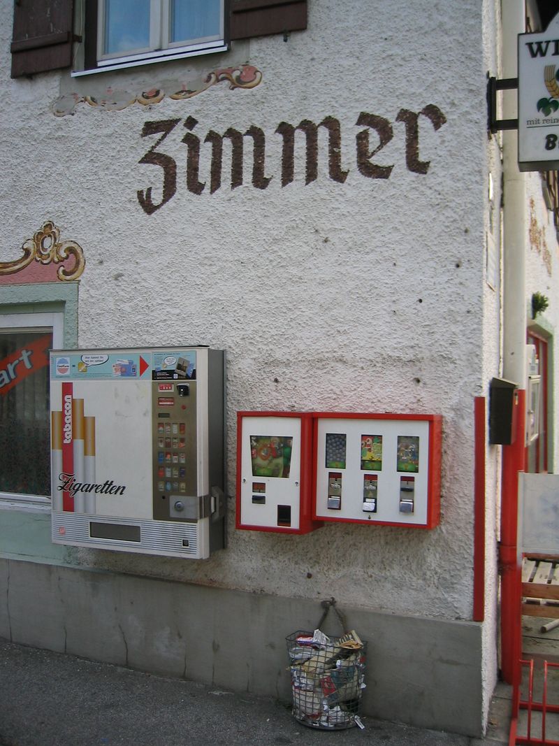 Rot-weiße Automaten an einer historischen Fassade mit Aufschrift „Zimmer“