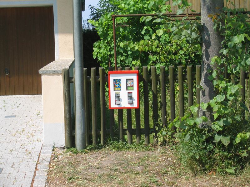 Rot-weißer Automat an einem Holzzaun im Grünen
