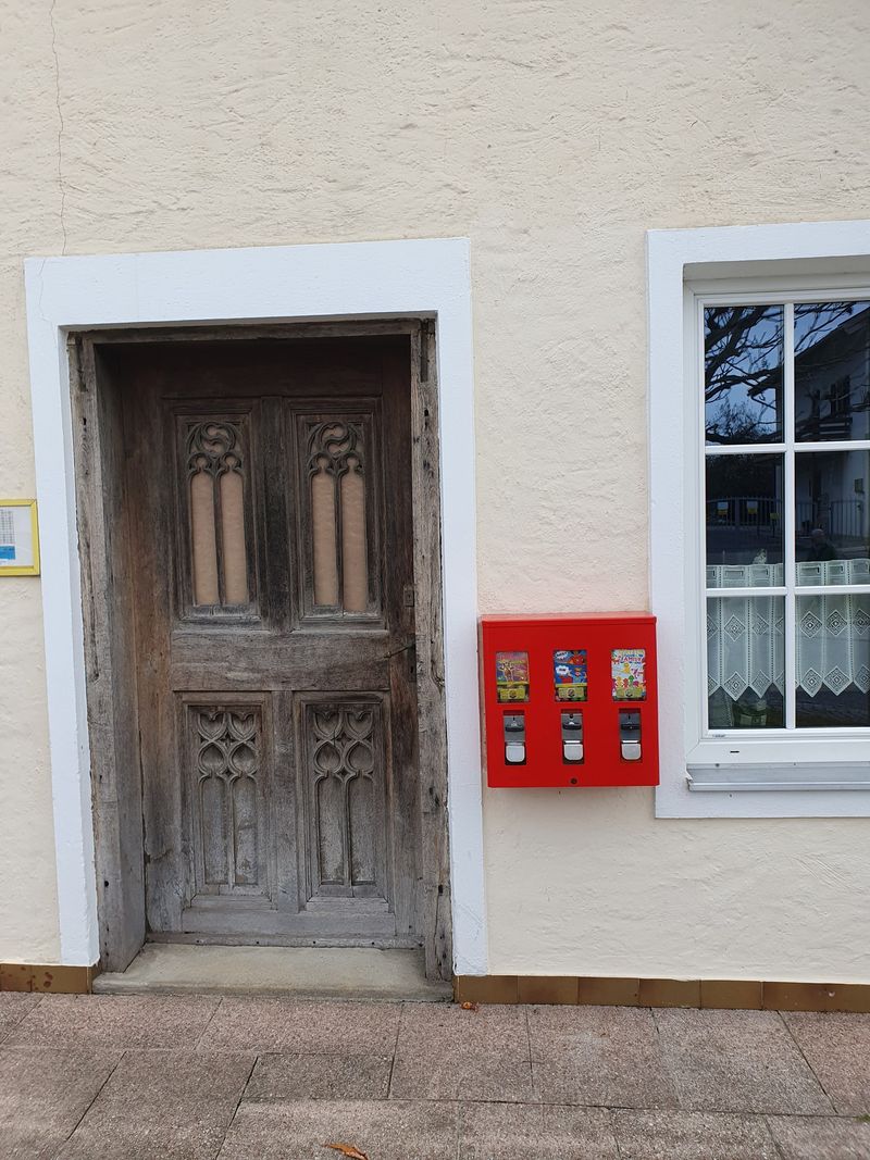 Kleiner roter Automat neben einer alten Holztür