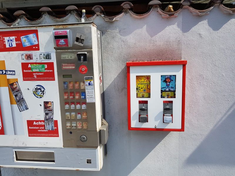 Rot-weißer Automat neben einem Zigarettenautomaten unter einem Vordach