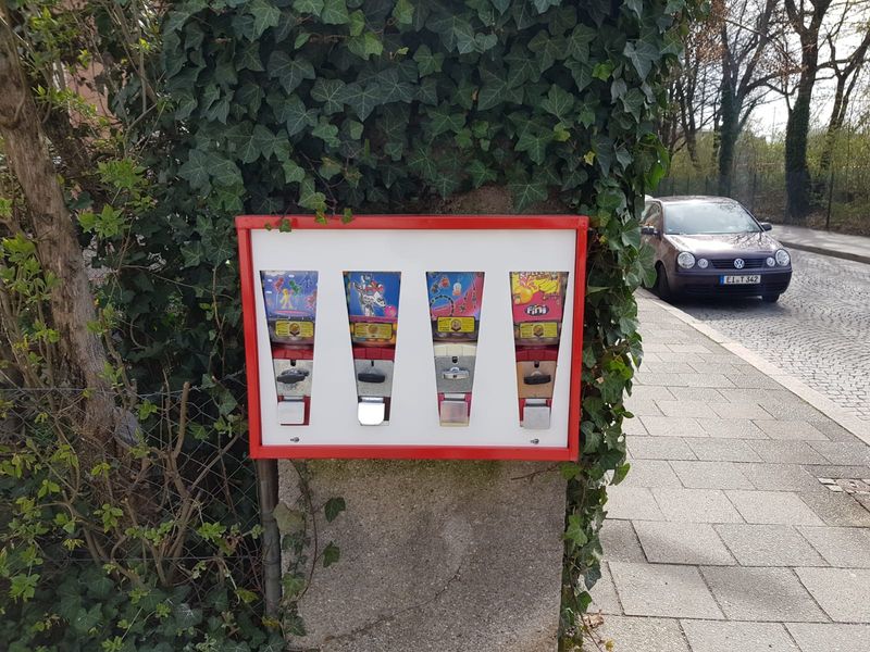 Vierfach-Automat mit bunten Füllungen an einer efeubewachsenen Mauer
