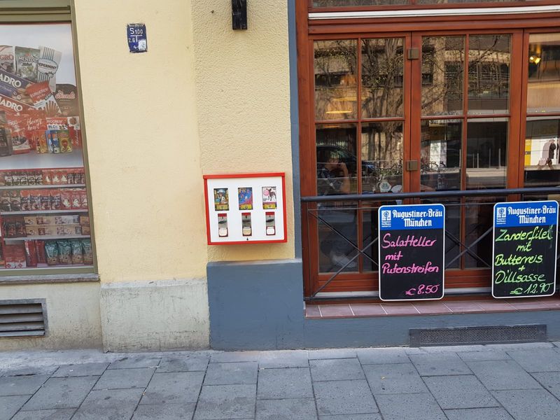 Rot-weißer Automat an der Fassade eines Lokals neben dem Fenster