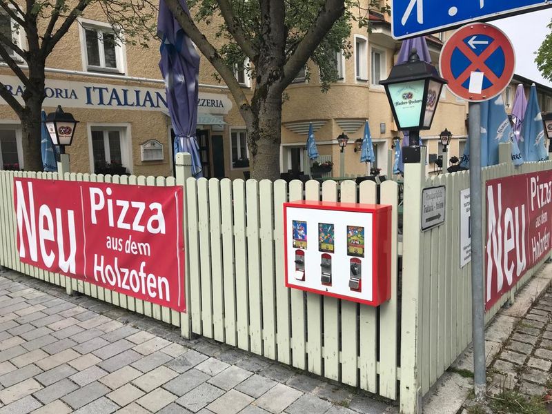 Automat an einem Holzzaun vor einer Pizzeria