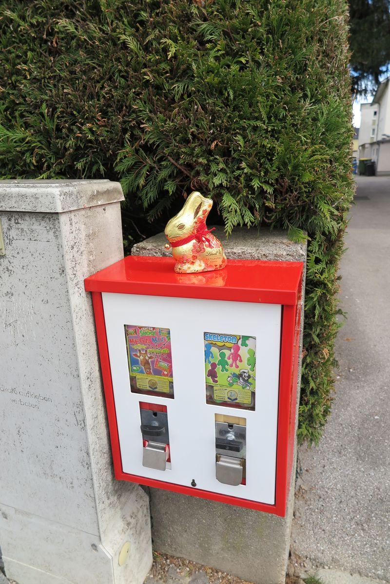 Rot-weißer Automat auf einem Mauerpfeiler, darauf ein Schokoladenhase