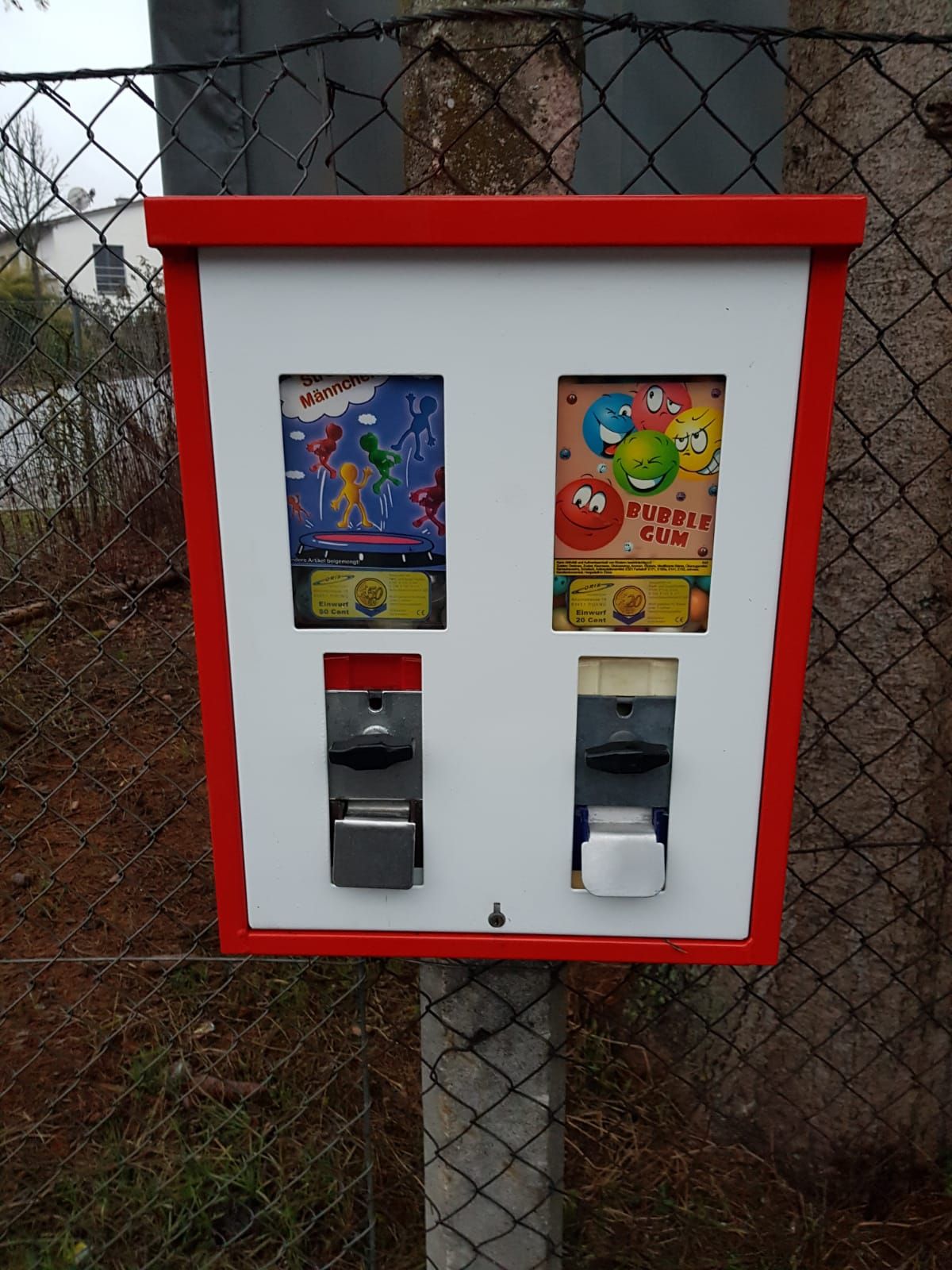 Rot-weißer Doppelautomat mit Spielzeug und Bubble Gum an einem Zaun