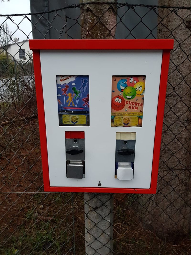 Rot-weißer Doppelautomat mit Spielzeug und Bubble Gum an einem Zaun