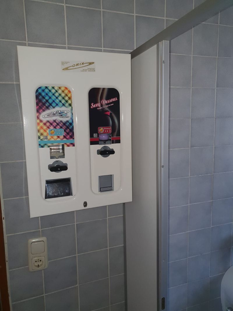 Nahaufnahme eines weißen Kondomautomaten mit zwei Schächten