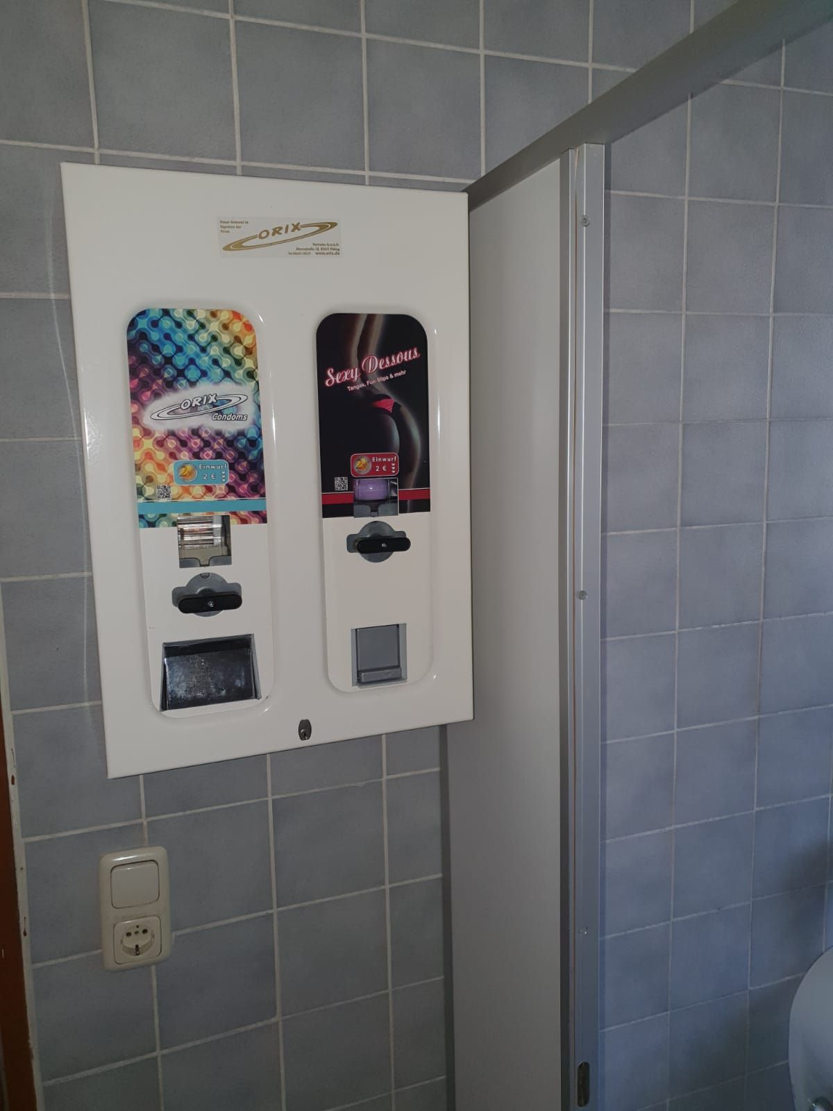 Nahaufnahme eines weißen Kondomautomaten mit zwei Schächten